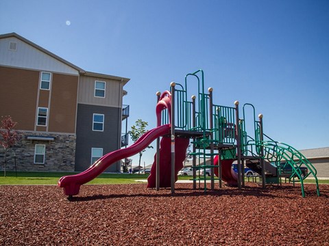a playground with a slide and climbing equipment in front of an apartment building