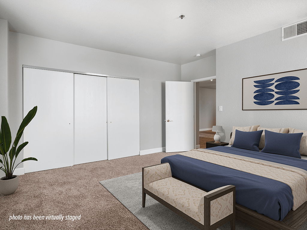 A bedroom with a bed, a bench, and a plant.