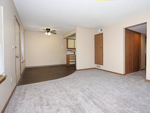 an empty living room with a ceiling fan and a door to a kitchen