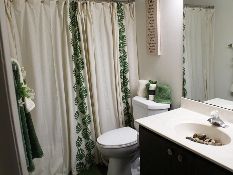 a bathroom with a white toilet next to a white sink with a green and white shower curtain
