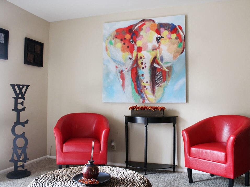 a living room with a large painting of an elephant on the wall and two red chairs