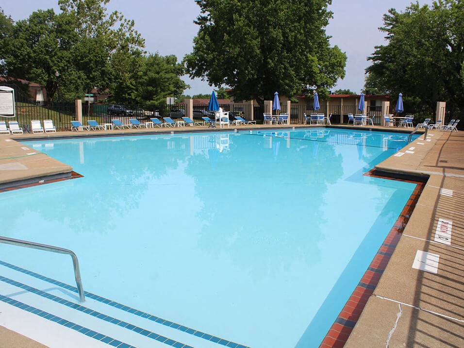 a large swimming pool with lounge chairs and trees in the background