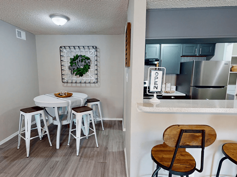 A kitchen with a table and chairs in the foreground and a kitchen in the background.