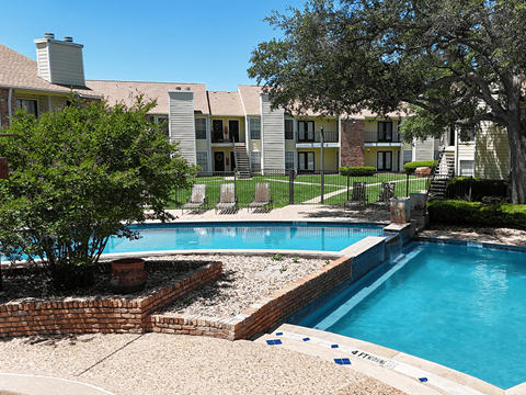 A pool surrounded by a brick wall and a tree.