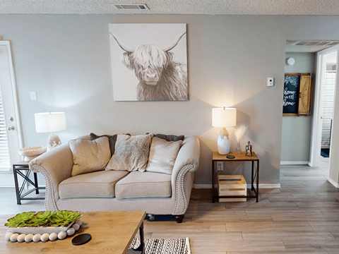A living room with a couch, a coffee table, and a painting of a cow on the wall.