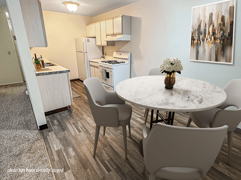 A kitchen with a table and chairs in the foreground and a refrigerator and cabinets in the background.