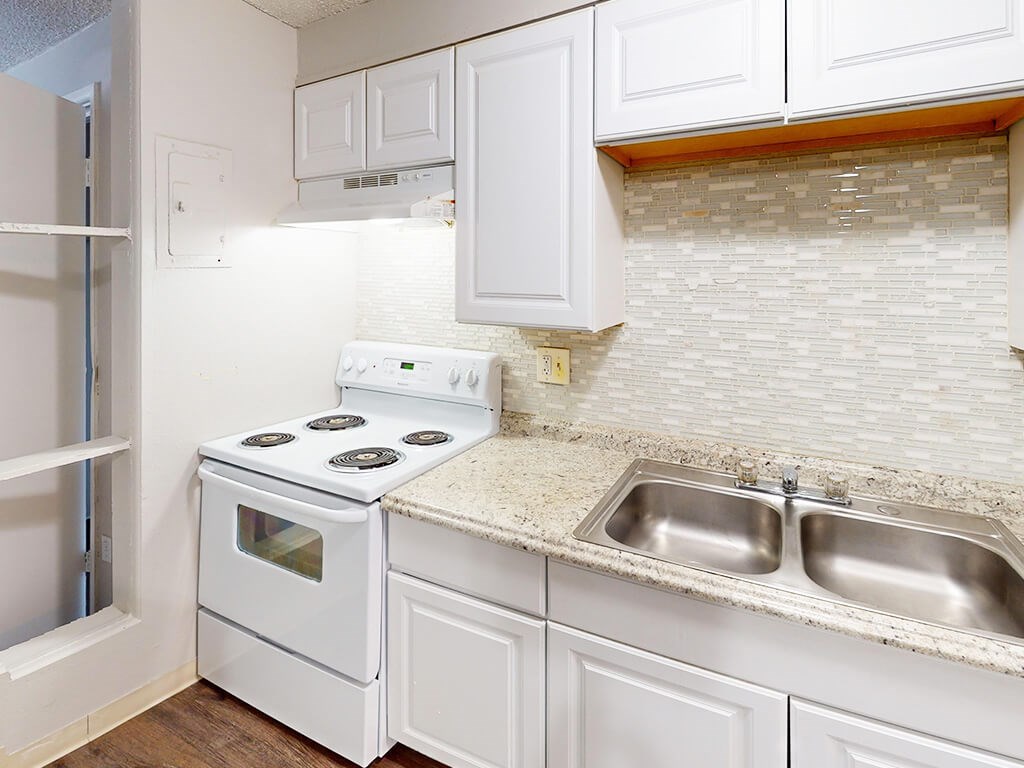 A white kitchen with a stove, sink, and cabinets.