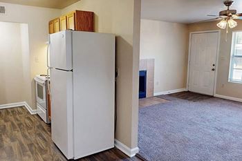 A white refrigerator with a wooden box on top sits in a room with a carpeted floor.
