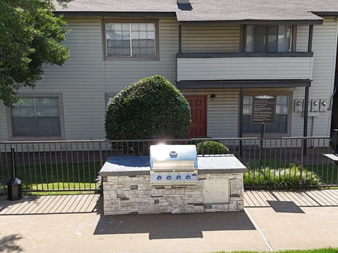 A stone and tile outdoor kitchen with a grill and sink.