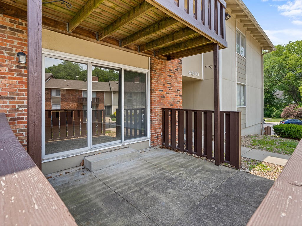 a porch in front of a brick apartment building with a sliding glass door