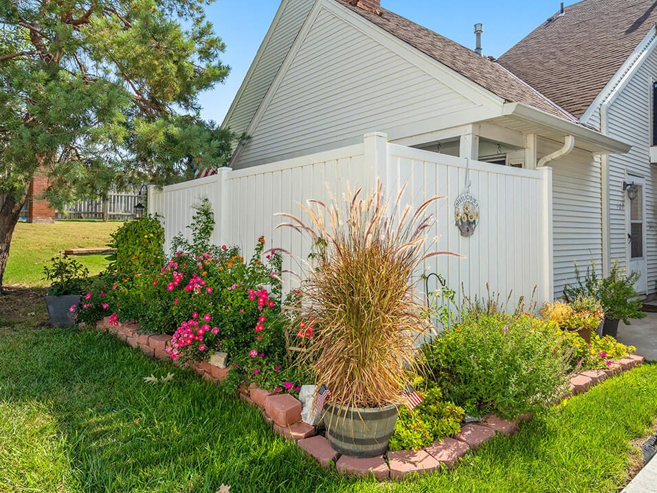 a garden in front of a house with a white fence