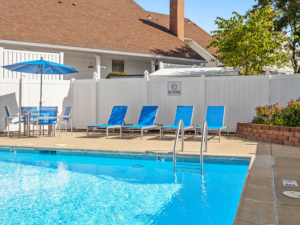 a swimming pool with blue chairs and umbrellas in front of a hotel pool