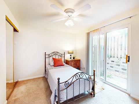A bedroom with a bed, a ceiling fan, and a sliding glass door.
