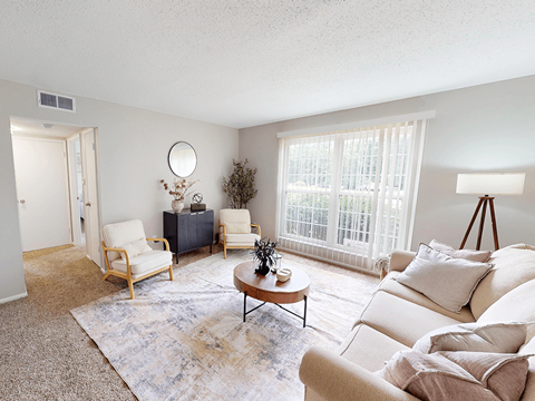 A living room with a white couch, a wooden coffee table, and a large window with white curtains.