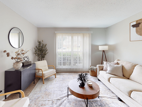 A living room with a white couch, a wooden coffee table, and a large window with white blinds.