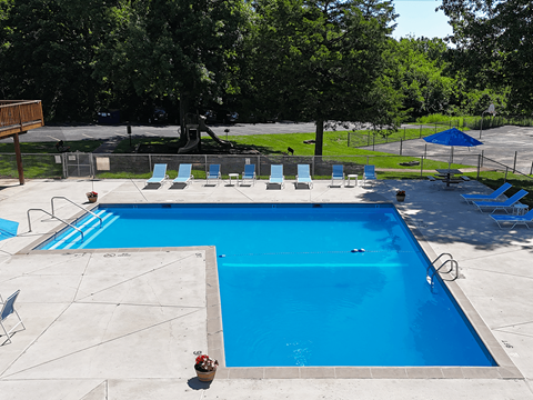 A large blue swimming pool surrounded by trees and chairs.