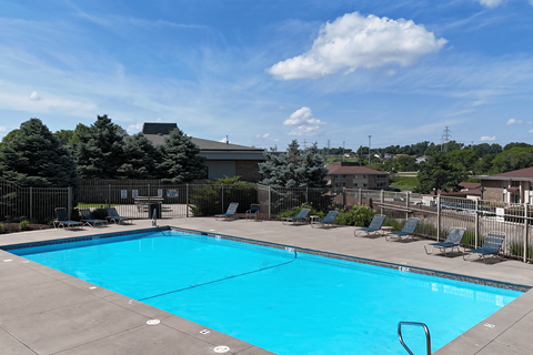 A large blue swimming pool surrounded by a fence and lounge chairs.