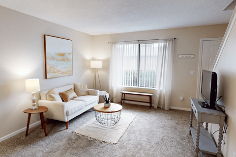 A living room with a white couch, a coffee table, a lamp, a painting, and a window with curtains.