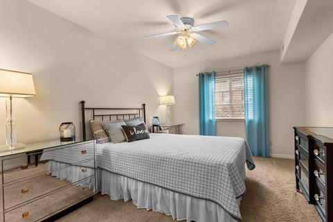 A bedroom with a bed, dresser, and ceiling fan.