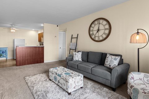 A living room with a grey couch, a clock on the wall, and a rug on the floor.