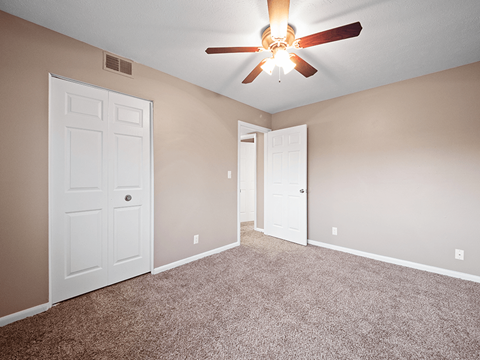 an empty bedroom with a ceiling fan and doors