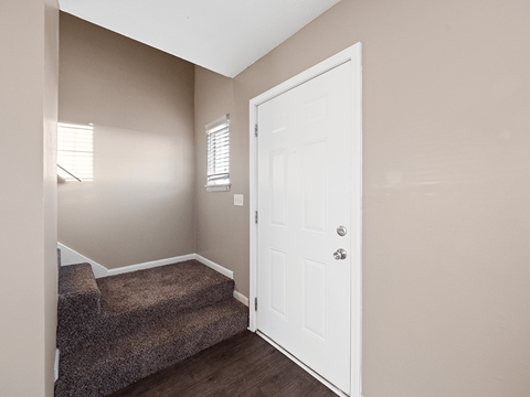 an empty entryway with a white door and carpeted stairs