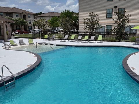 A swimming pool with a black fence and green chairs.