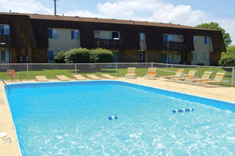 A swimming pool in front of a building with sun loungers on the side.