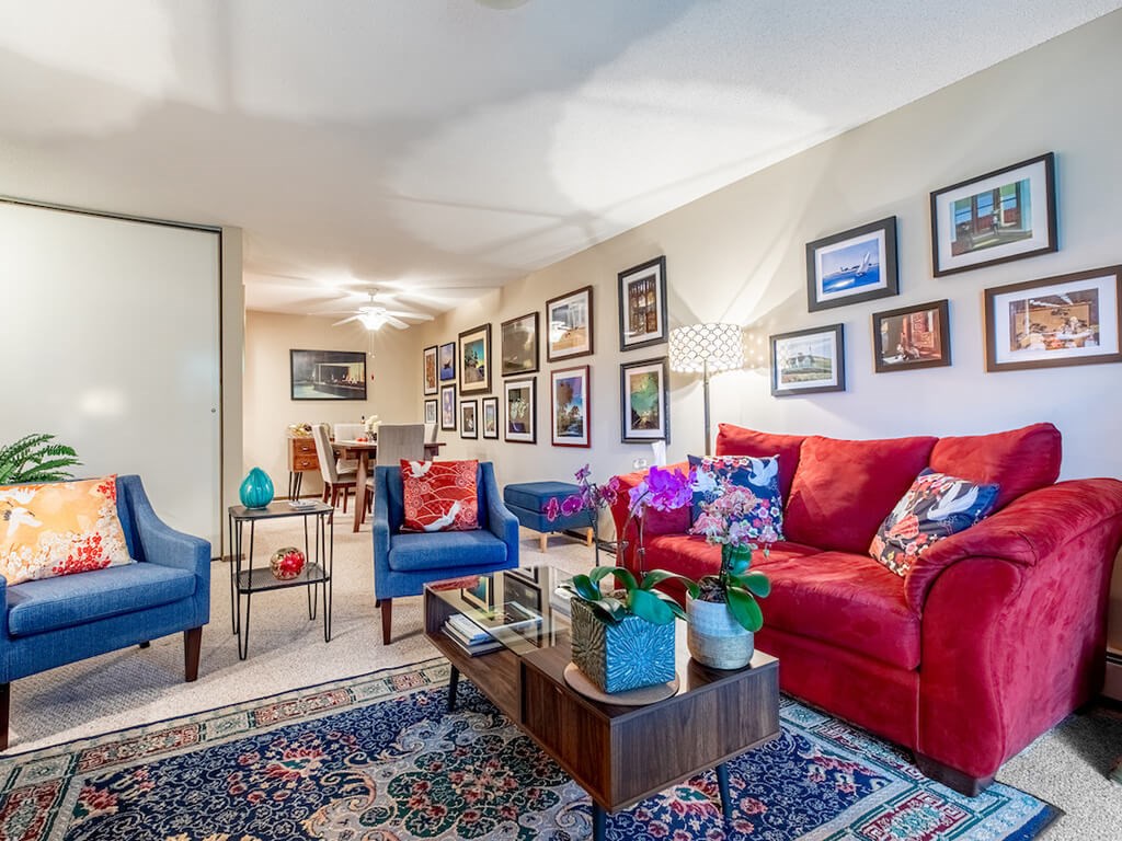 A living room with a red couch, blue chairs, and pictures on the wall.