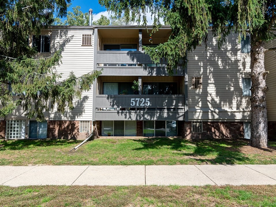 an apartment building with a sidewalk and trees in front of it