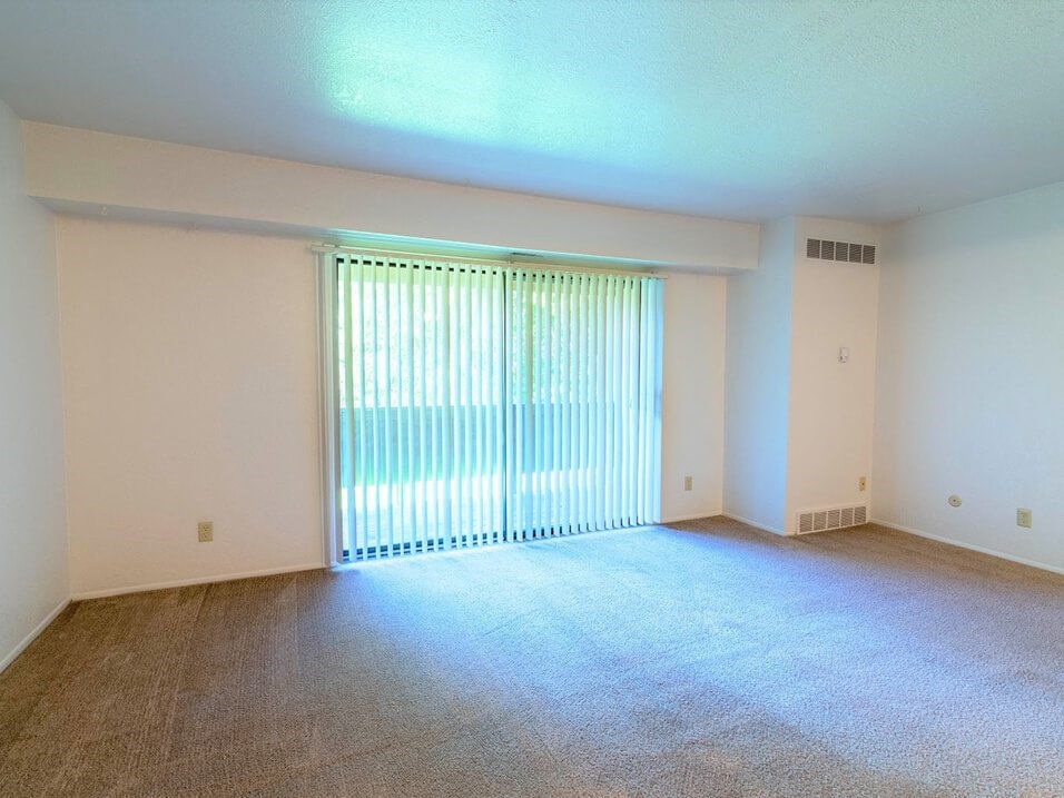 an empty living room with a large window and carpeting