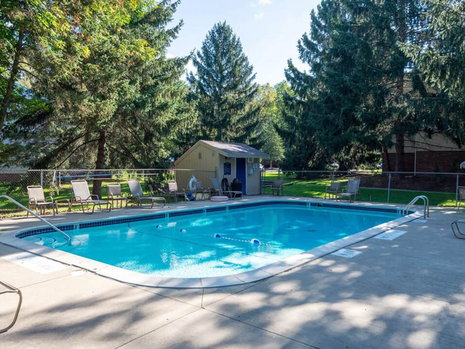 a swimming pool with chairs around it and trees in the background