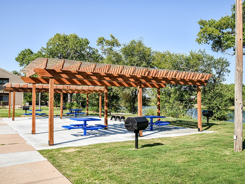 A wooden pergola with blue picnic tables underneath it.