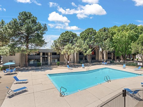 a picture of swimming pool with trees and a blue sky above it