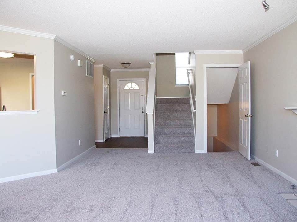 an empty living room with a white carpet and a staircase