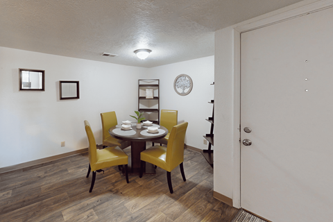 A dining room with a table set for two and yellow chairs.