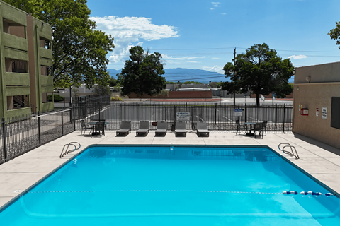 A blue swimming pool surrounded by a black fence and chairs.