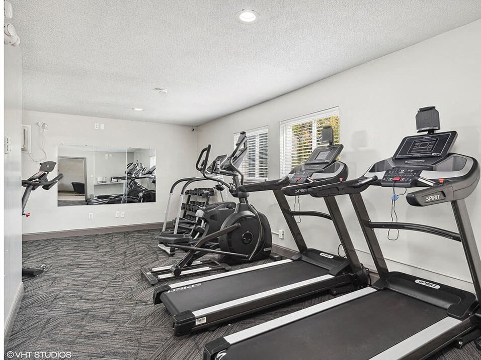 the gym in the home has cardio equipment and a large mirror