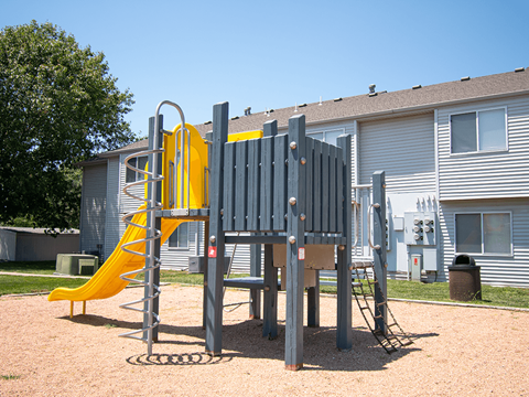 A playground with a yellow slide and a grey play structure.