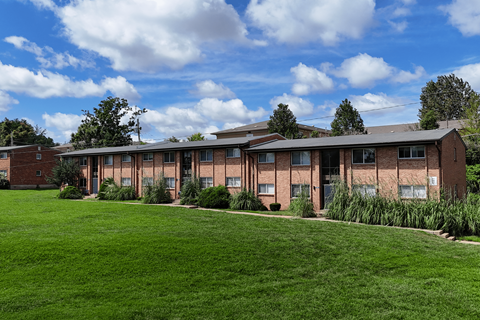 A large grassy area in front of a building with a blue sky and clouds in the background.