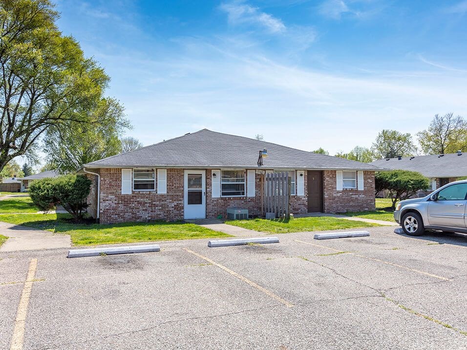 a small brick house with a car parked in a parking lot