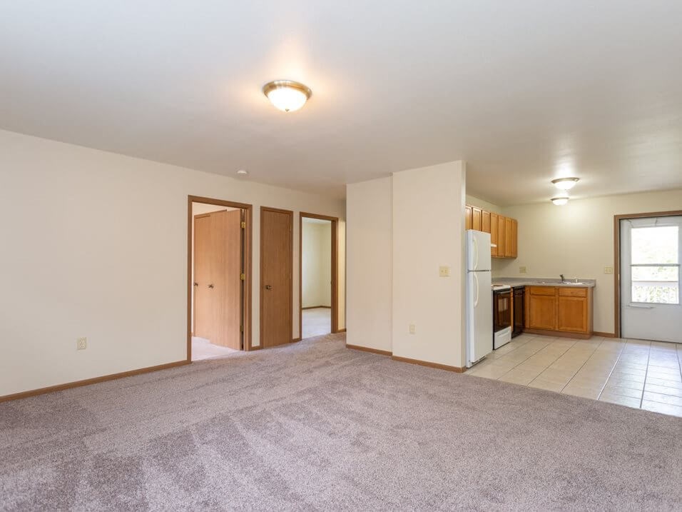 an empty living room with a kitchen in the background