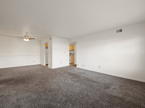 A spacious room with a carpeted floor and a ceiling fan.
