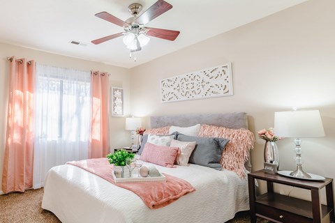 A bedroom with a bed, a fan, and a nightstand with a lamp.