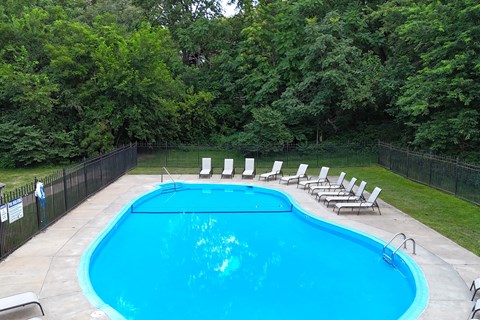 A pool surrounded by trees and chairs.