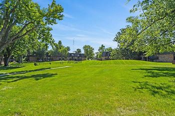 a field of green grass with trees and buildings