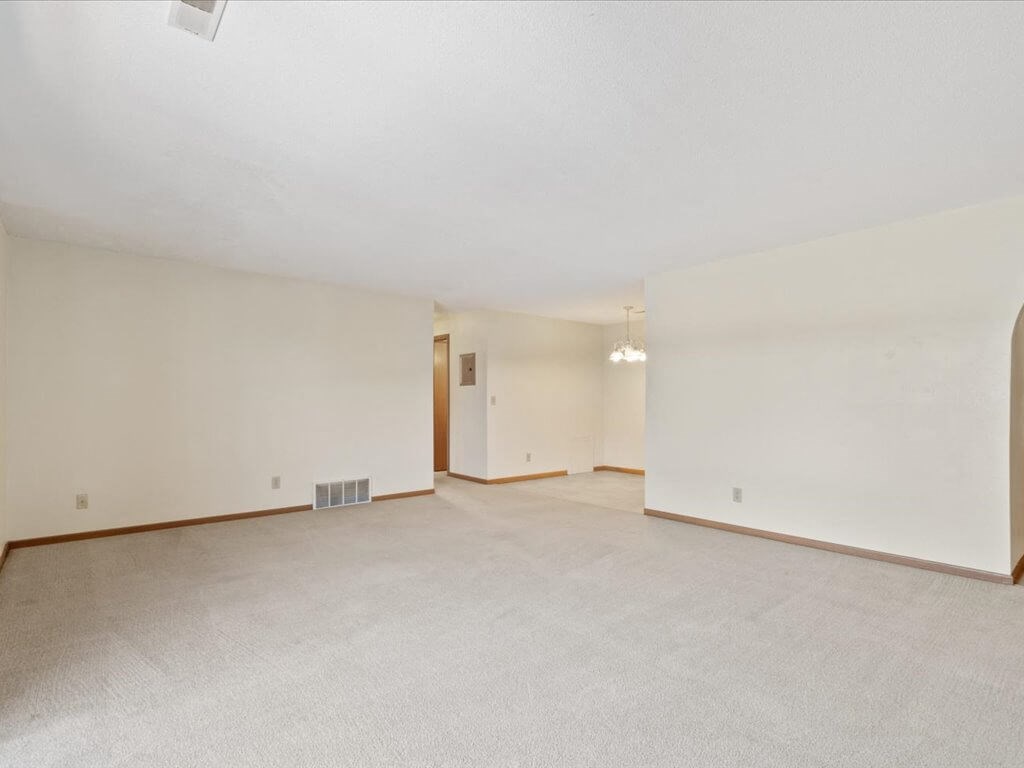 the living room and dining room of an empty home with white walls and carpet