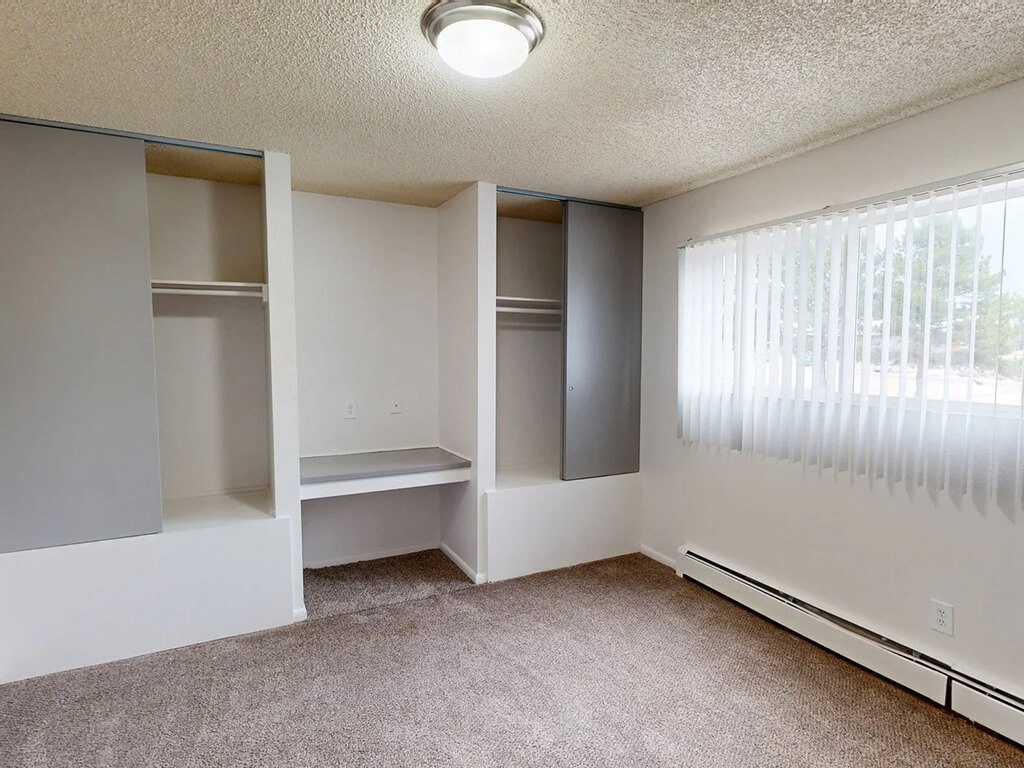 A room with a carpeted floor and a window with blinds.