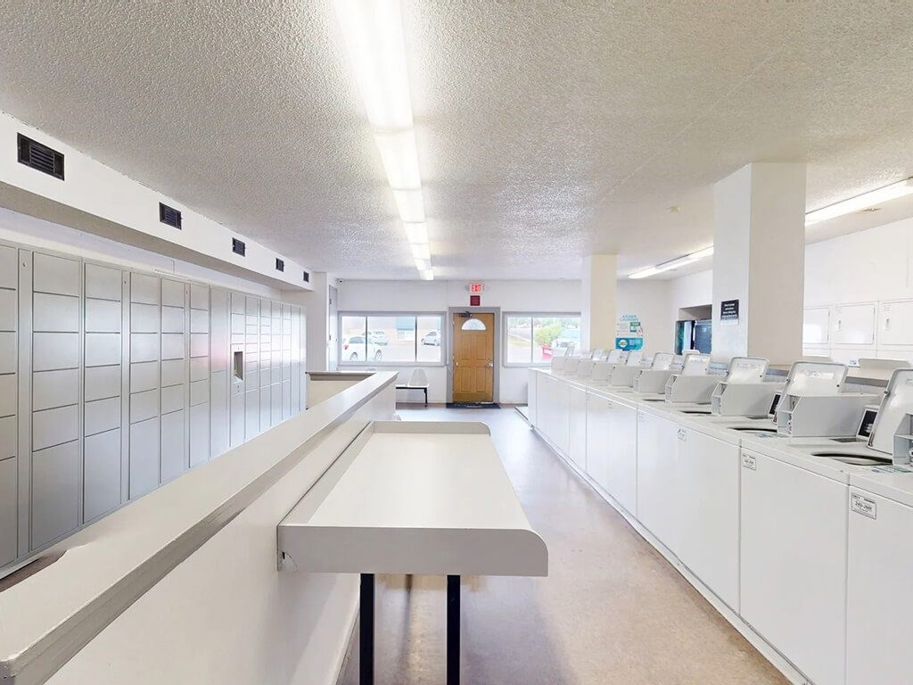 A long white table is in the middle of a room with white cabinets on the walls.