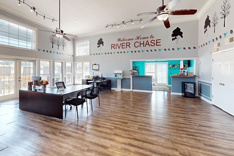 A spacious room with a black table and chairs, a ceiling fan, and a sign that reads "Welcome Home to River Chase.".